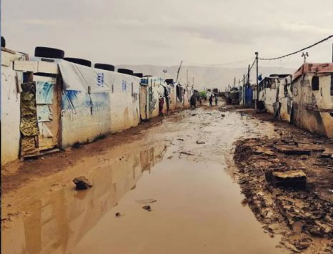 A flooded, muddy street between tents in a Syrian refugee camp after snowmelt