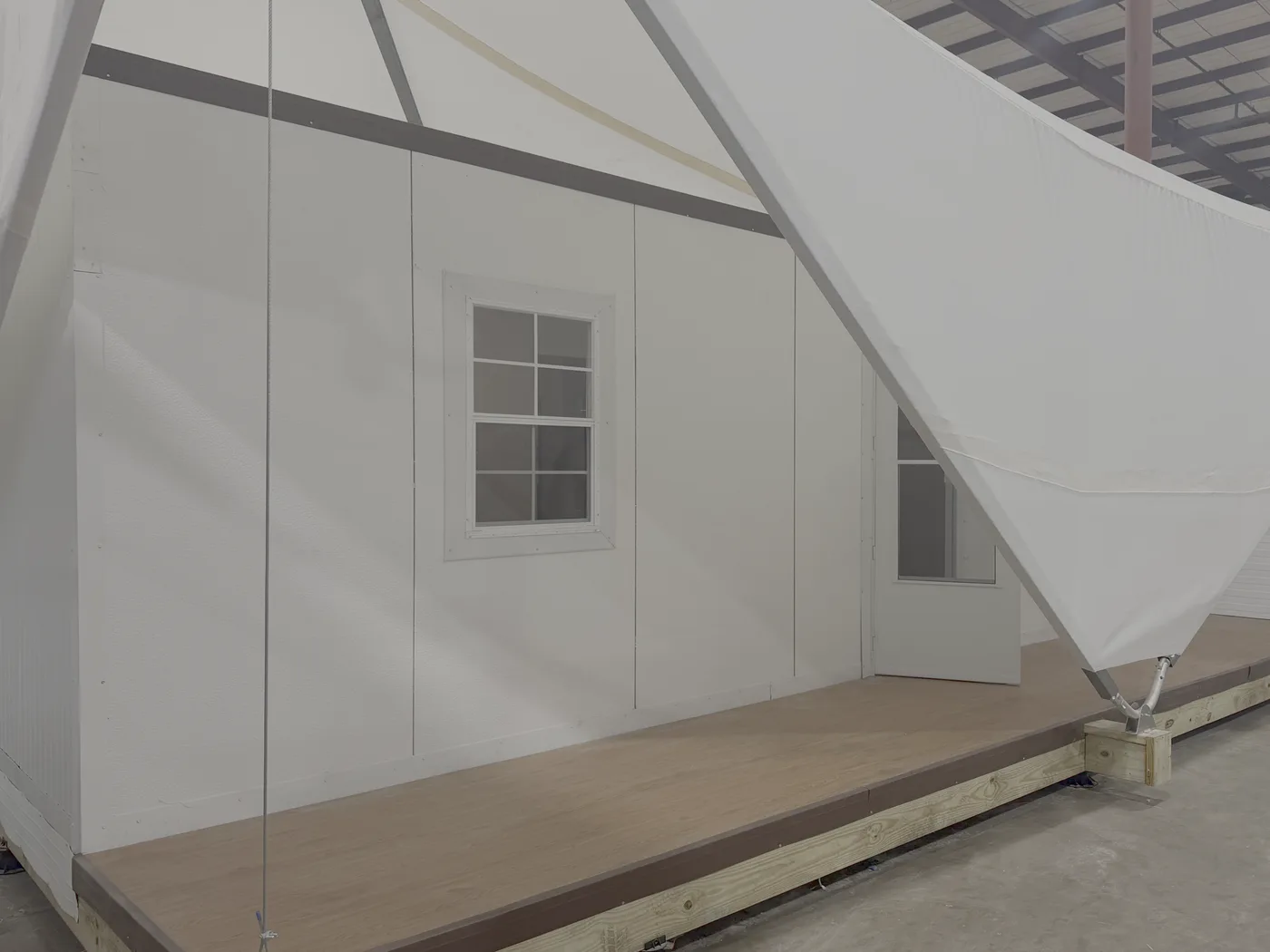 An Estia Home prototype assembled, with the panelled wall, window and door facing a raised timber deck, and the fabric canopy drawn down to an anchor at the near corner